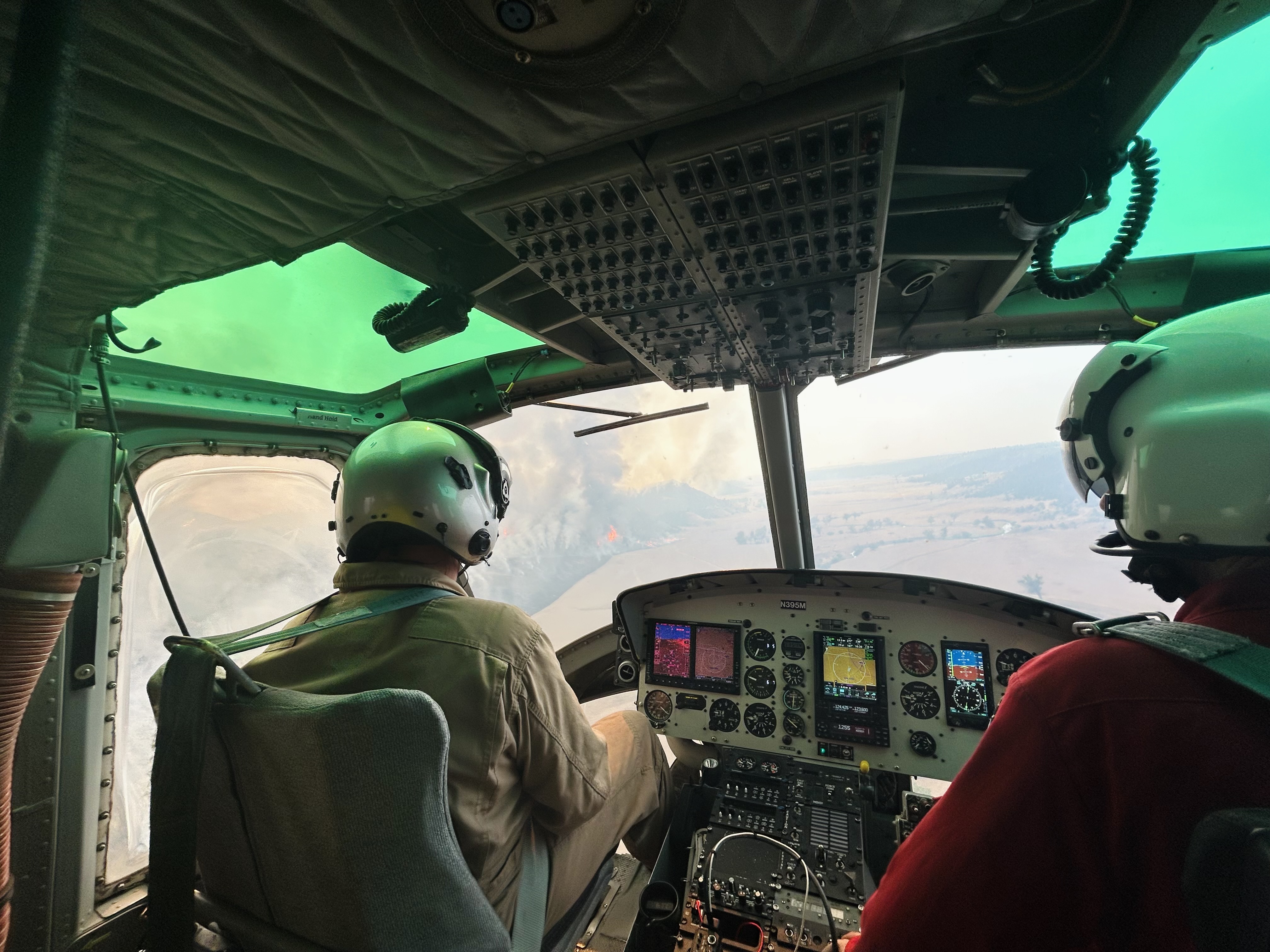 Pilots in cockpit fly toward smoke plume from active wildfire.