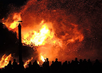 Large flames burning in the background with the silhouette of people in the foreground. 