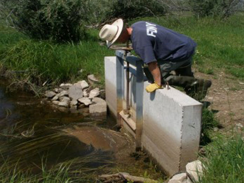 A man is leaning over adjusting a headgate on a ditch